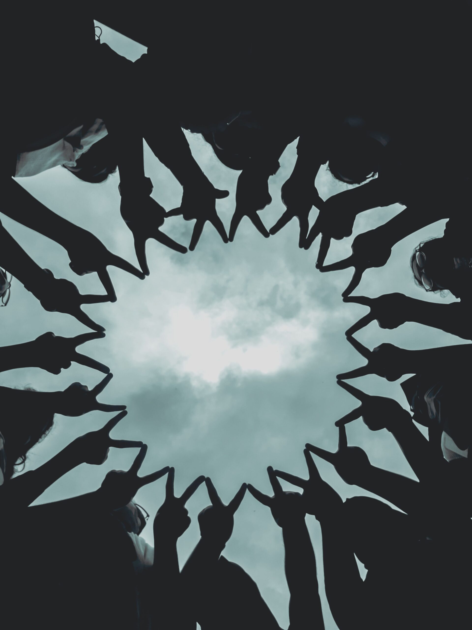 Silhouette of people forming a star with hands against a cloudy sky.